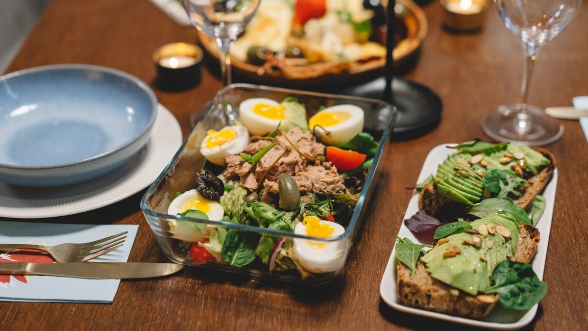 Elegant dining setup with fresh salad, avocado toast, and wine glasses on a wooden table.